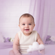 Close-up portrait of a happy baby with a slight smile, against a soft lavender and bright white background.